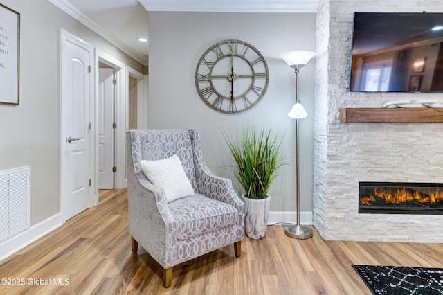 living area featuring hardwood / wood-style floors, ornamental molding, and a stone fireplace