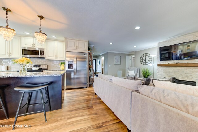 kitchen featuring light stone counters, hanging light fixtures, light wood-type flooring, backsplash, and appliances with stainless steel finishes