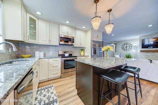 kitchen with appliances with stainless steel finishes, pendant lighting, a breakfast bar, light stone counters, and sink