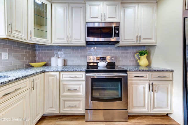 kitchen with light stone counters, appliances with stainless steel finishes, cream cabinets, and tasteful backsplash