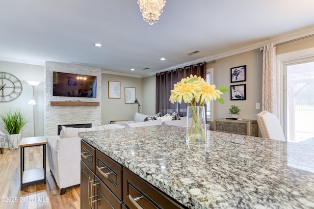 kitchen featuring a stone fireplace, light wood-type flooring, light stone countertops, ornamental molding, and dark brown cabinets