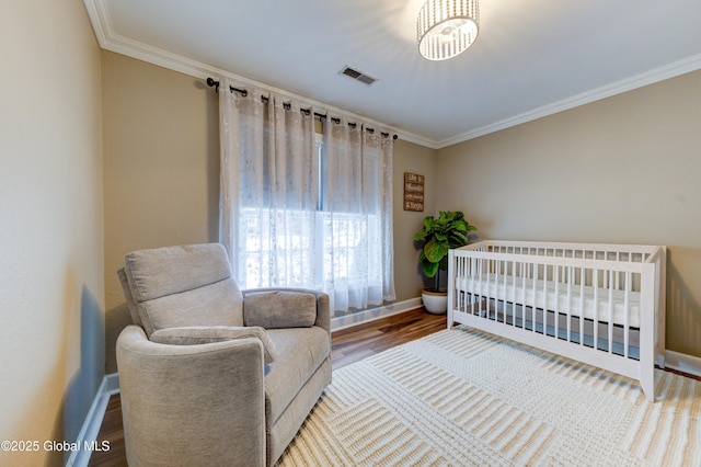 bedroom featuring hardwood / wood-style floors, a nursery area, and ornamental molding