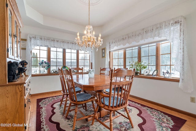 dining space featuring light hardwood / wood-style floors, a tray ceiling, and a notable chandelier