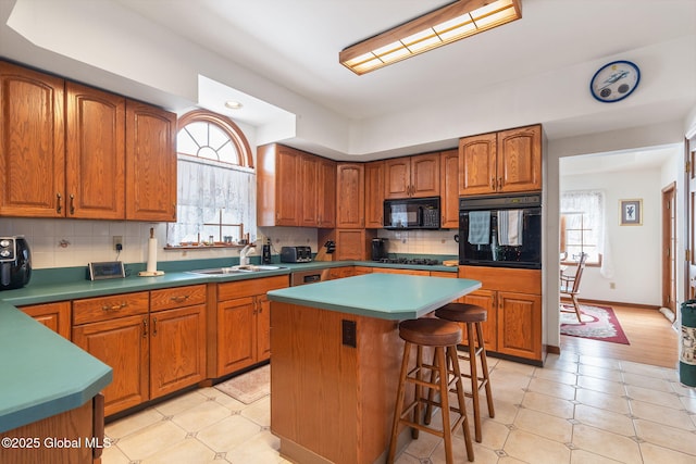 kitchen featuring a center island, black appliances, sink, tasteful backsplash, and a breakfast bar area