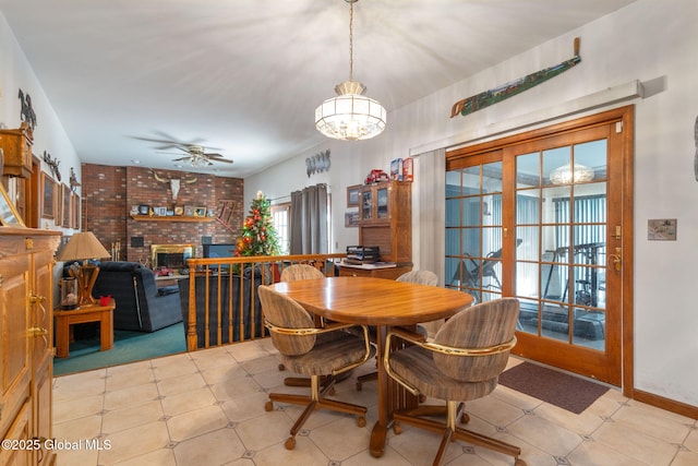 dining area with ceiling fan with notable chandelier, french doors, brick wall, and a brick fireplace