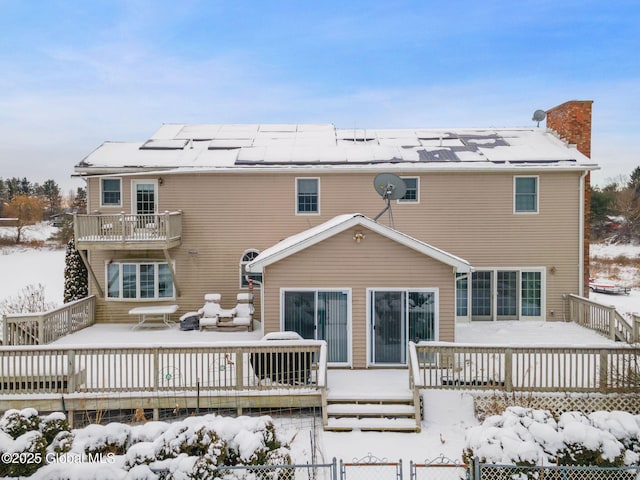 snow covered property with solar panels, a balcony, and a wooden deck