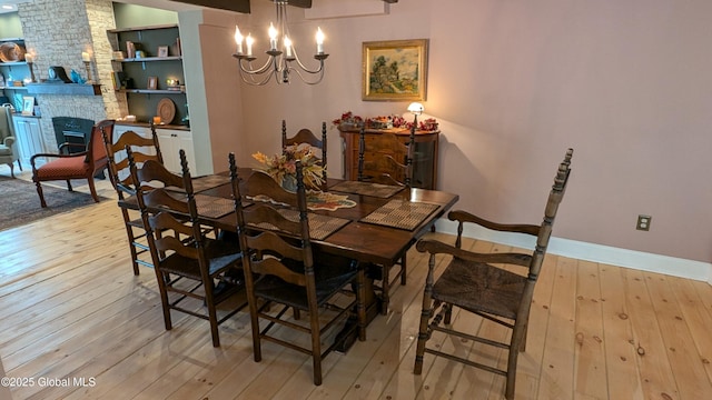 dining area featuring a notable chandelier, a stone fireplace, and light wood-type flooring