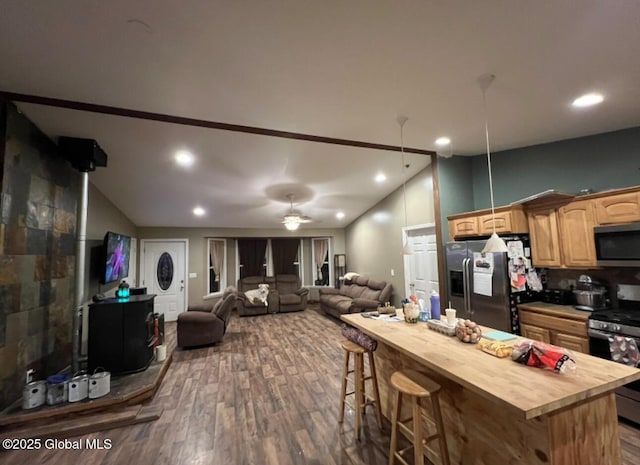 kitchen featuring wood counters, dark wood-type flooring, a kitchen breakfast bar, ceiling fan, and stainless steel appliances