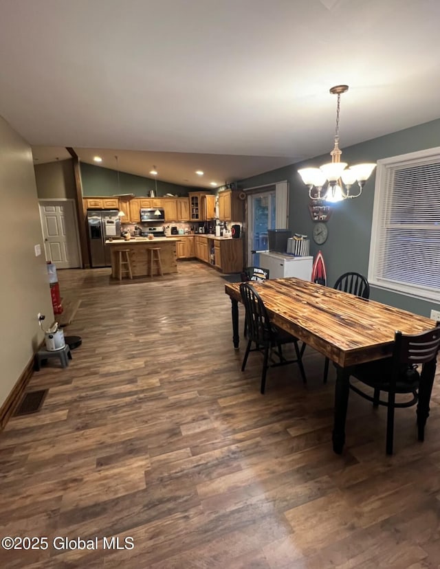 dining area with dark wood-type flooring, a chandelier, and lofted ceiling