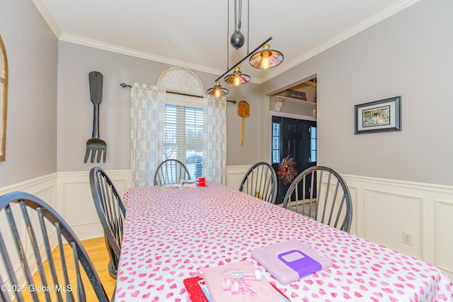 dining room featuring ornamental molding, a wainscoted wall, wood finished floors, and a decorative wall