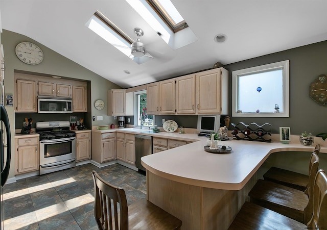 kitchen with kitchen peninsula, light brown cabinets, ceiling fan, lofted ceiling with skylight, and appliances with stainless steel finishes