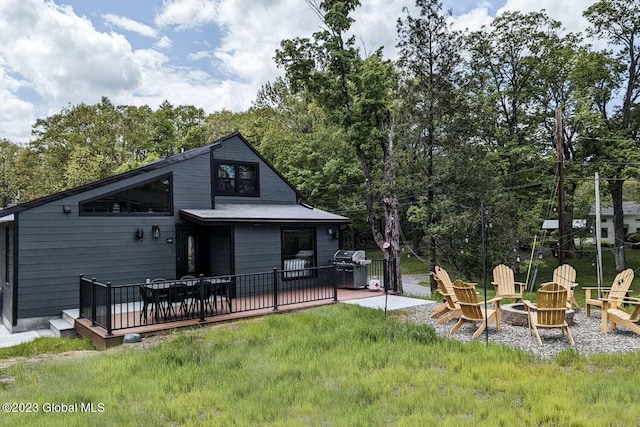 rear view of property with a wooden deck, a yard, and an outdoor fire pit