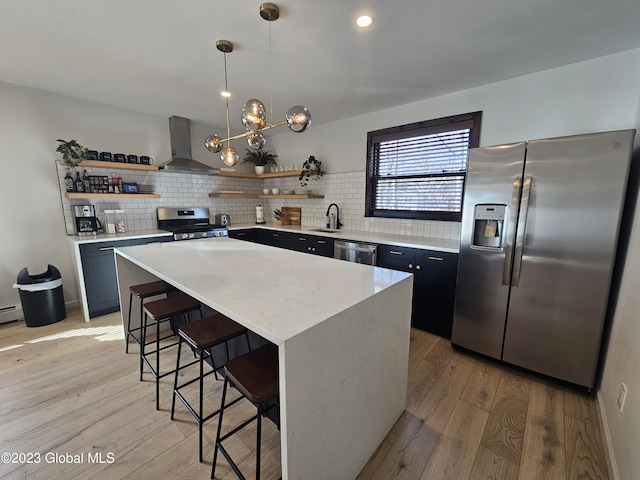 kitchen featuring wall chimney exhaust hood, a kitchen island, decorative backsplash, and appliances with stainless steel finishes