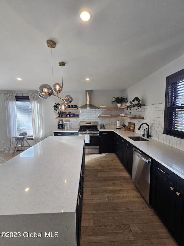 kitchen with sink, hanging light fixtures, stainless steel appliances, wall chimney range hood, and backsplash