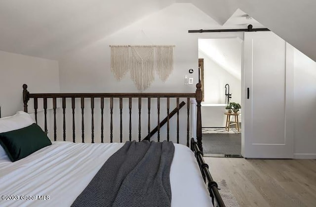 bedroom featuring hardwood / wood-style floors, a barn door, and lofted ceiling