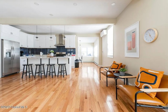 kitchen with white cabinetry, hanging light fixtures, wall chimney range hood, tasteful backsplash, and stainless steel refrigerator with ice dispenser