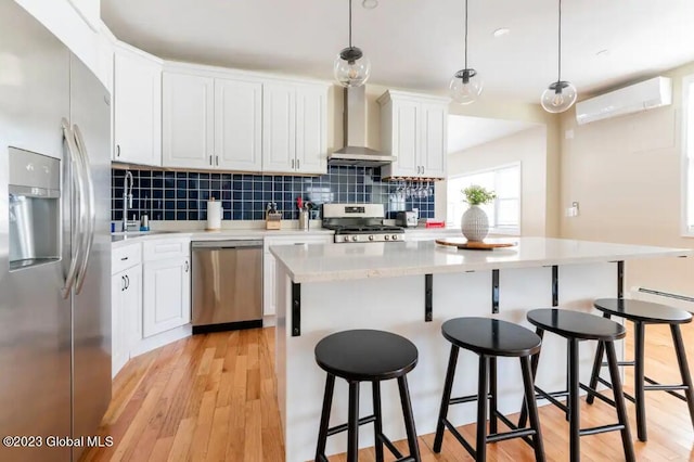 kitchen with white cabinets, wall chimney exhaust hood, stainless steel appliances, and decorative light fixtures