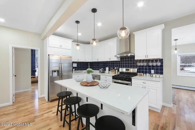 kitchen featuring white cabinets, wall chimney exhaust hood, pendant lighting, and appliances with stainless steel finishes