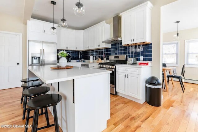 kitchen featuring white cabinetry, decorative light fixtures, stainless steel appliances, and wall chimney range hood