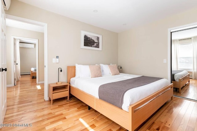 bedroom featuring wood-type flooring, baseboard heating, and a wall mounted AC