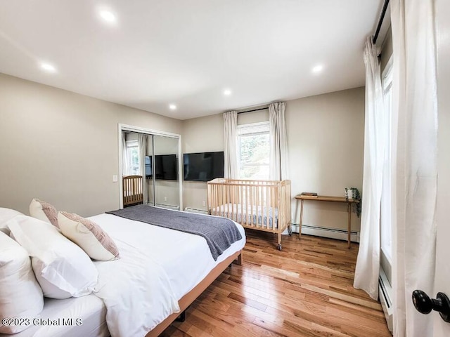 bedroom with wood-type flooring, a baseboard radiator, and multiple windows