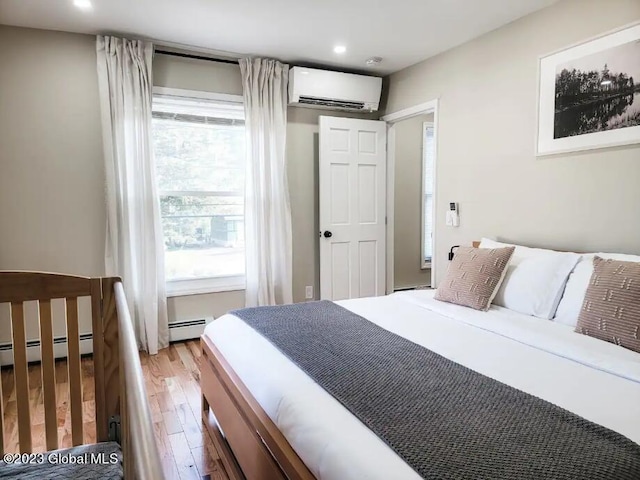 bedroom featuring an AC wall unit, wood-type flooring, and baseboard heating