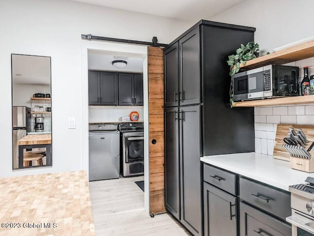 kitchen with decorative backsplash, stainless steel appliances, a barn door, separate washer and dryer, and light hardwood / wood-style flooring