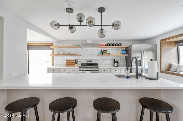 kitchen with a breakfast bar, sink, wall chimney exhaust hood, appliances with stainless steel finishes, and kitchen peninsula