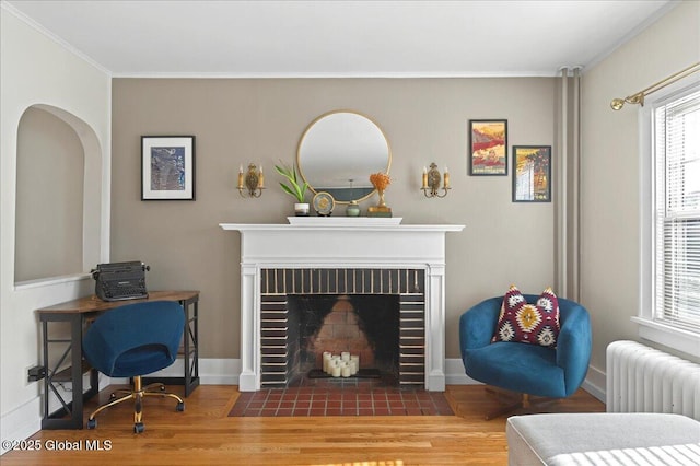 living room with a brick fireplace, radiator, baseboards, ornamental molding, and wood finished floors