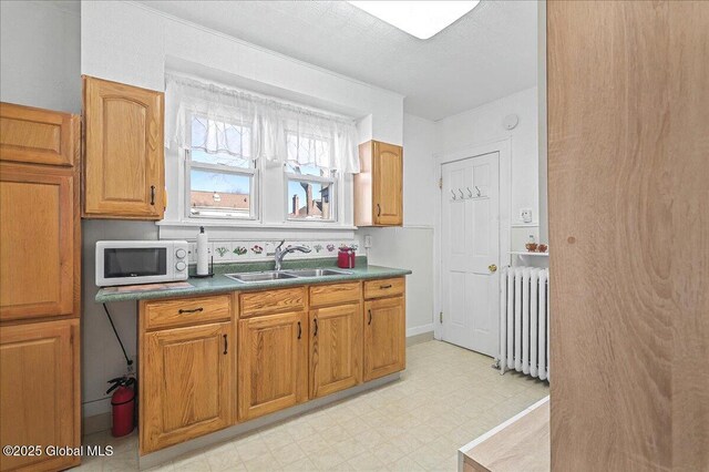 kitchen with a sink, light floors, radiator, brown cabinetry, and white microwave