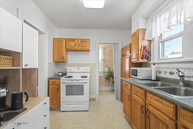 kitchen featuring a sink, dark countertops, white appliances, brown cabinetry, and light floors