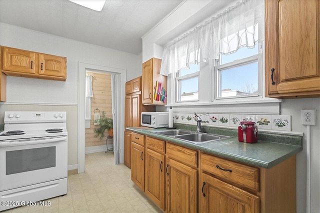 kitchen with white appliances, brown cabinetry, light floors, a sink, and dark countertops