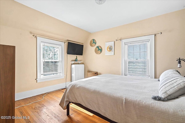 bedroom featuring lofted ceiling, radiator, wood finished floors, and baseboards