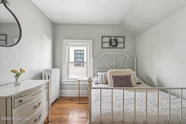 bedroom with baseboards, radiator, hardwood / wood-style floors, and vaulted ceiling