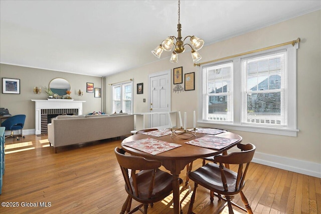 dining space with light wood-style flooring, a fireplace, baseboards, and a chandelier