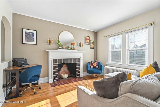 living room featuring wood finished floors, arched walkways, radiator, baseboards, and a brick fireplace