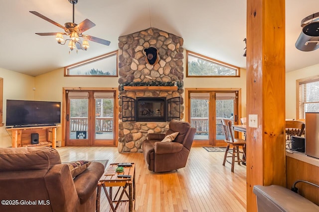 living room with ceiling fan, hardwood / wood-style floors, high vaulted ceiling, and a stone fireplace