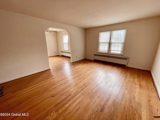 empty room featuring light hardwood / wood-style flooring, radiator, and ceiling fan