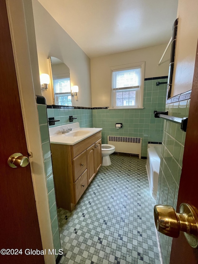 bathroom featuring radiator heating unit, toilet, a bathtub, vanity, and tile walls