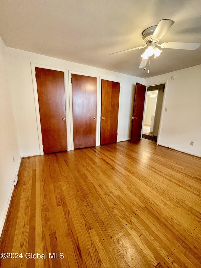 unfurnished bedroom featuring ceiling fan, light hardwood / wood-style floors, and two closets