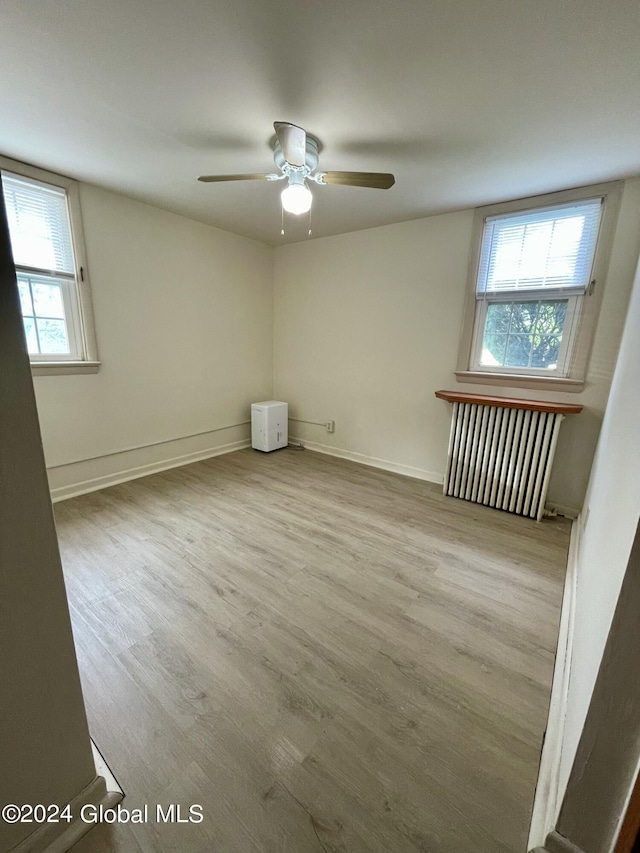 unfurnished room with radiator, ceiling fan, plenty of natural light, and light wood-type flooring