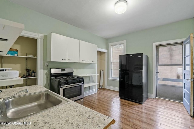 kitchen featuring white cabinets, black fridge, sink, light hardwood / wood-style flooring, and gas stove