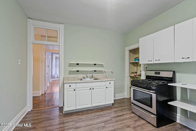 kitchen with sink, stainless steel gas range oven, light stone counters, hardwood / wood-style floors, and white cabinets