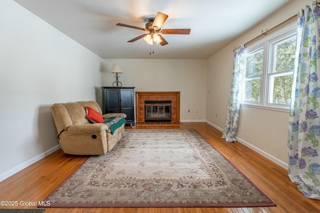 living area featuring ceiling fan, wood-type flooring, and a tile fireplace