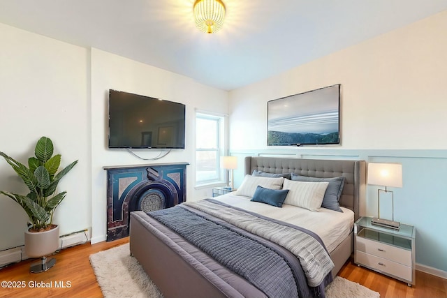 bedroom featuring a baseboard heating unit, a fireplace, and light wood-type flooring