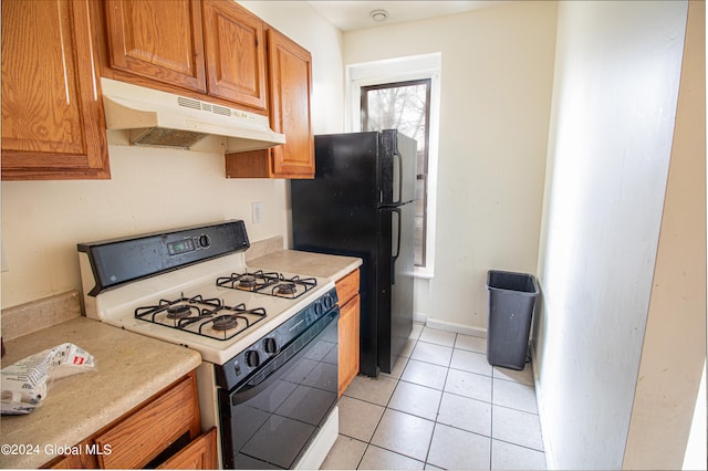 kitchen featuring white range with gas stovetop, light tile patterned floors, and black fridge