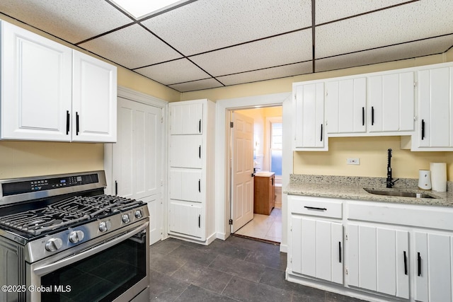 kitchen featuring white cabinets, a paneled ceiling, gas stove, and sink