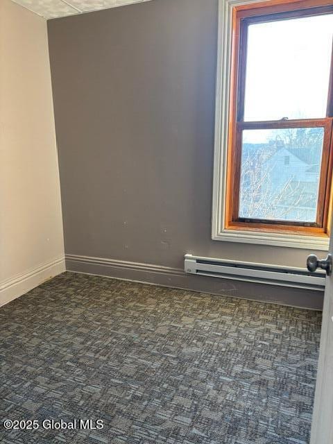 carpeted spare room with a baseboard heating unit