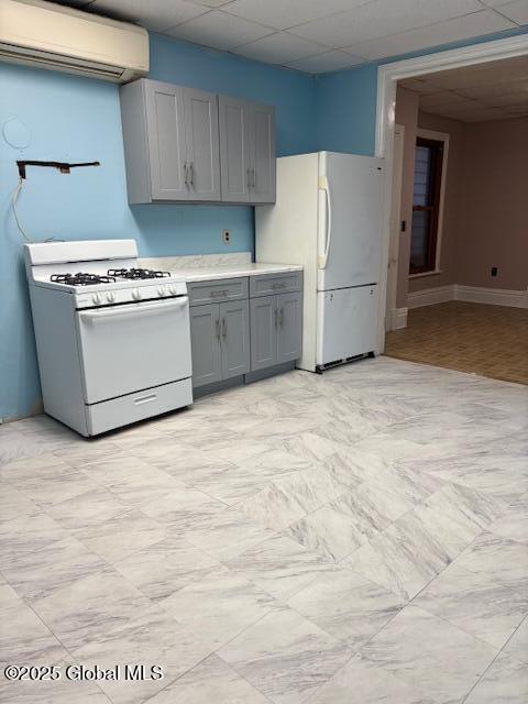 kitchen featuring an AC wall unit, gray cabinetry, a paneled ceiling, and white appliances