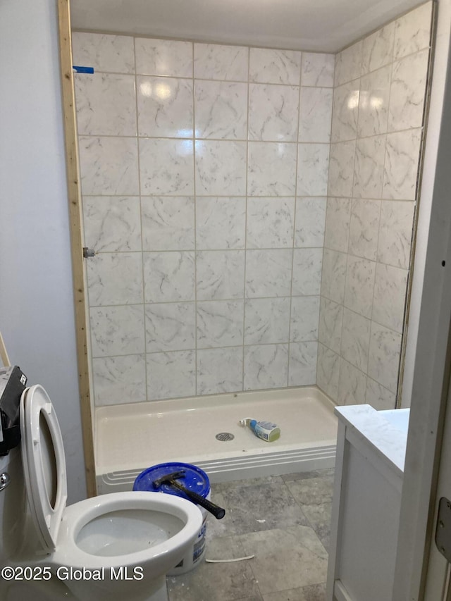 bathroom with a tile shower, vanity, and toilet